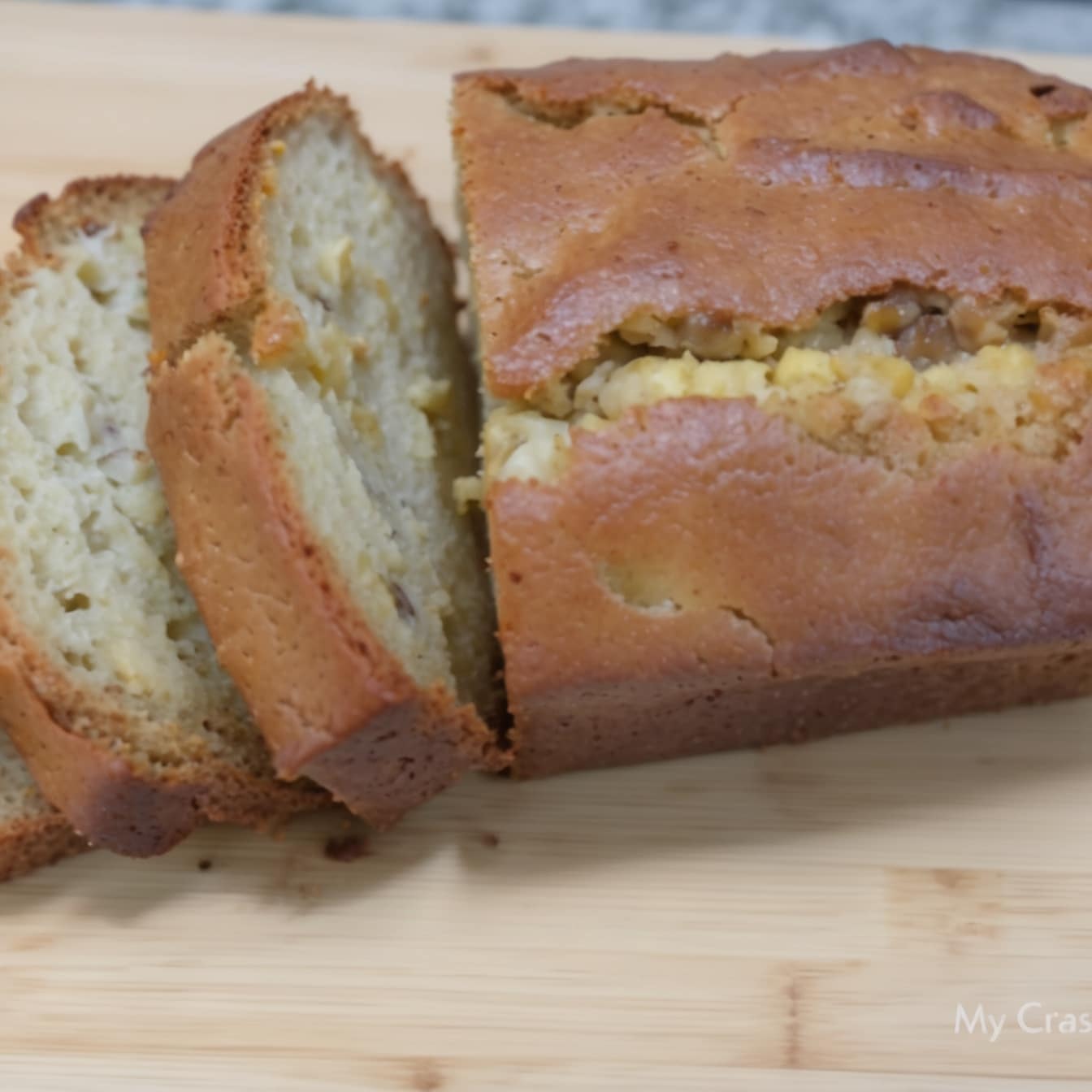 A loaf of Hawaiian banana bread partially sliced on a wooden cutting board.