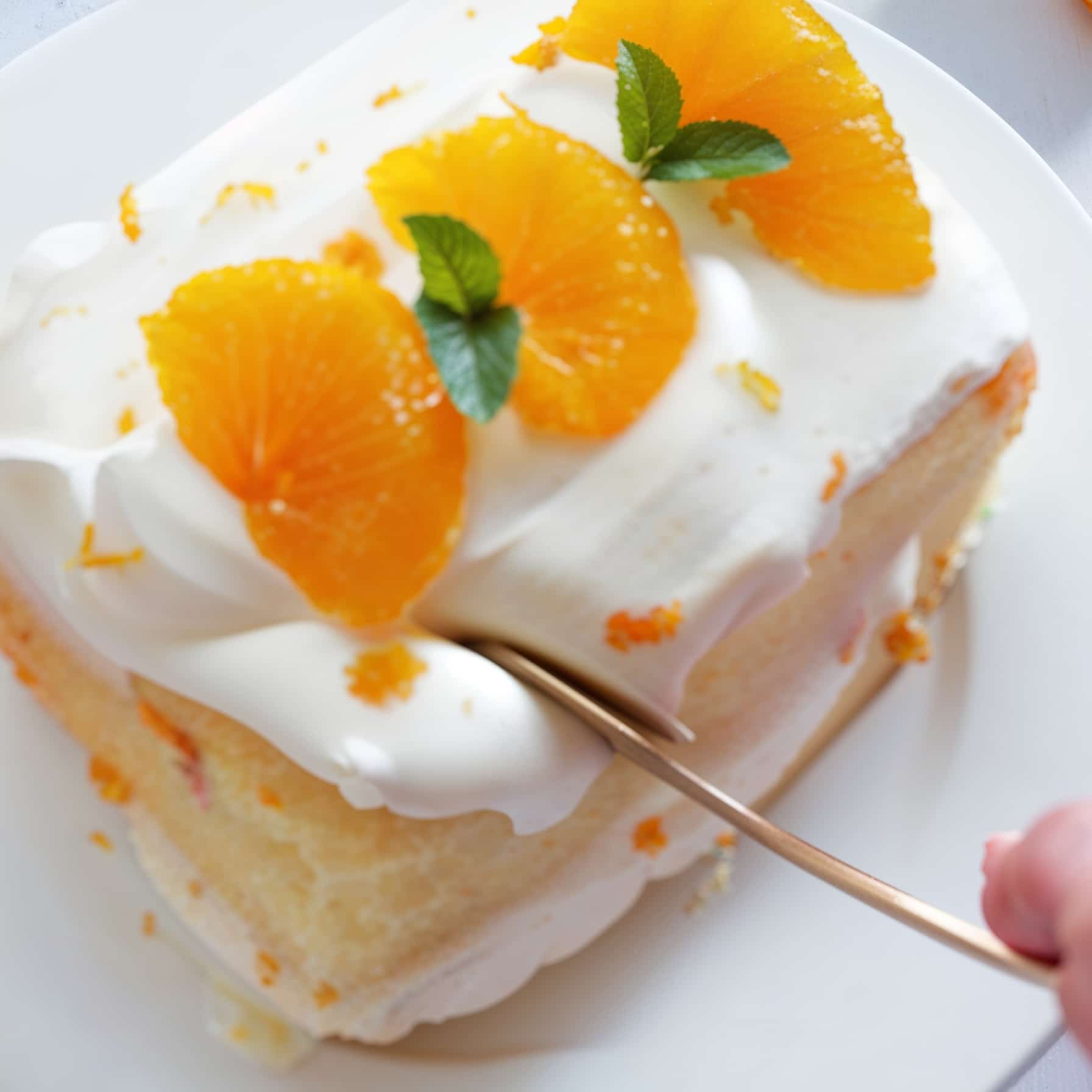 A slice of moist mandarin orange cake topped with fluffy frosting, fresh orange segments, and mint leaves