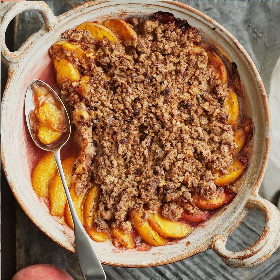 A freshly baked peach crumble in a rustic dish with a spoon scooping a serving.